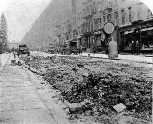 An old picture depicting an inner-city street filled with dirt.